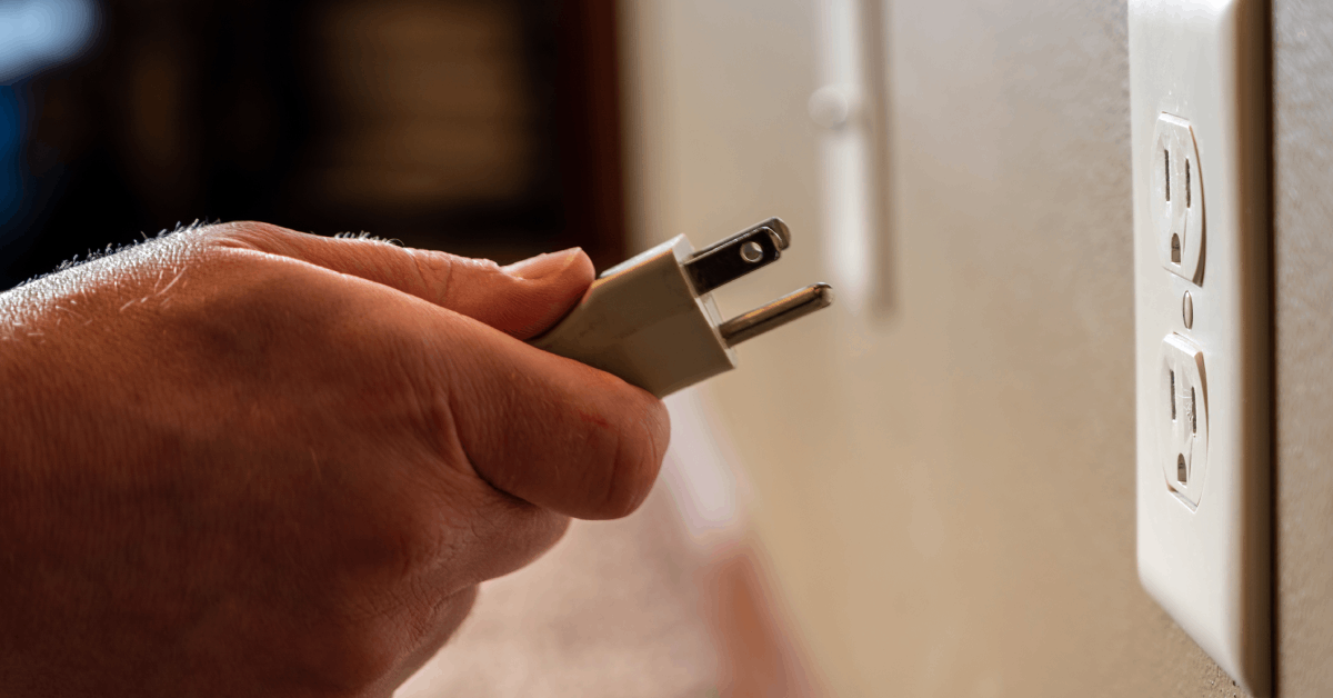 A person has unplugged a white three-pronged power cord from the wall outlet and holds it in his hands.