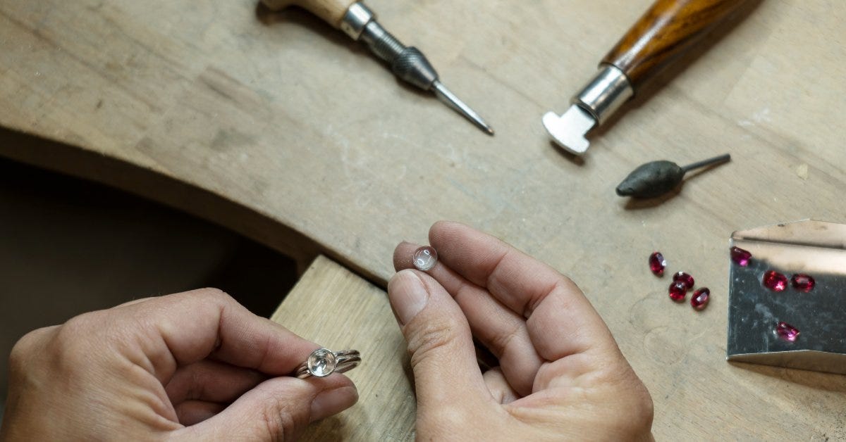 A jeweler examines a transparent stone before fixing it on the bezel of a silver ring at their workspace.