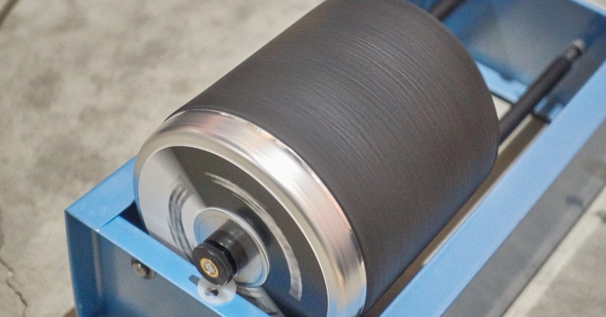 A blue rock tumbler machine with a barrel in motion sits by itself. Light reflects from its metal surfaces.