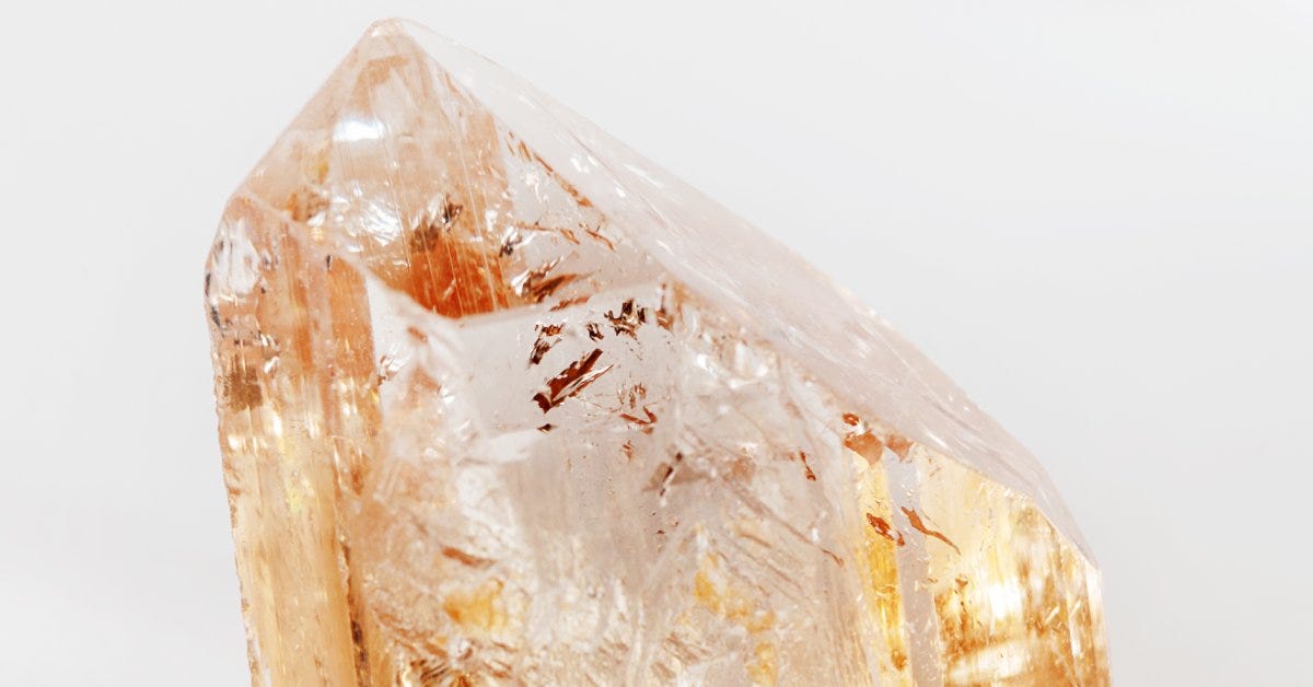  A topaz fragment rests on a white surface. The mineral's natural crevices and light orange color shine beautifully.