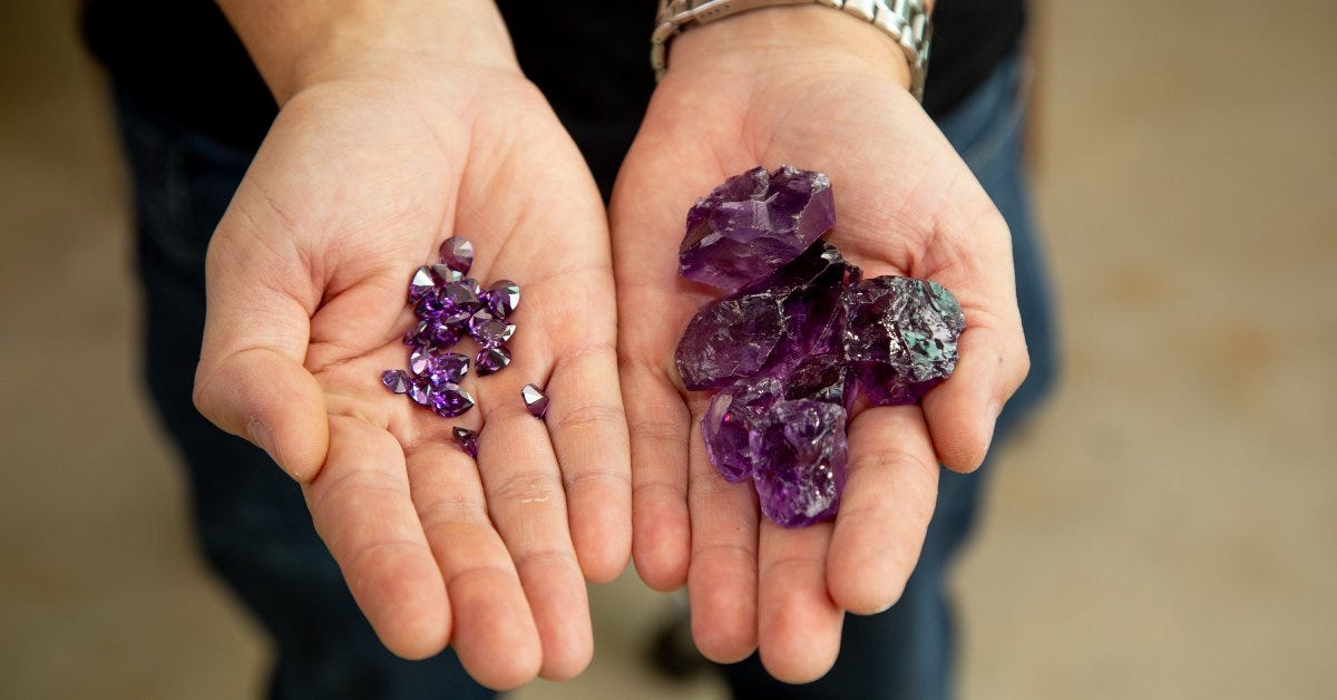 A person extends their hands with shiny purple gems in their palms. One hand holds larger stones and the other holds smaller ones.