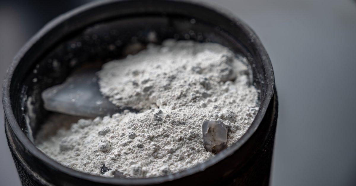 A rubber barrel is filled almost to the top with soft media for polishing clear gemstones under natural lighting.