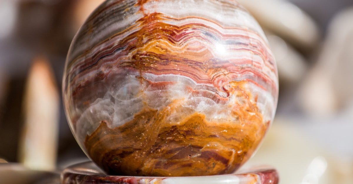 A jasper stone sphere rests on a matching base. An overhead light source reflects on its detailed surface.