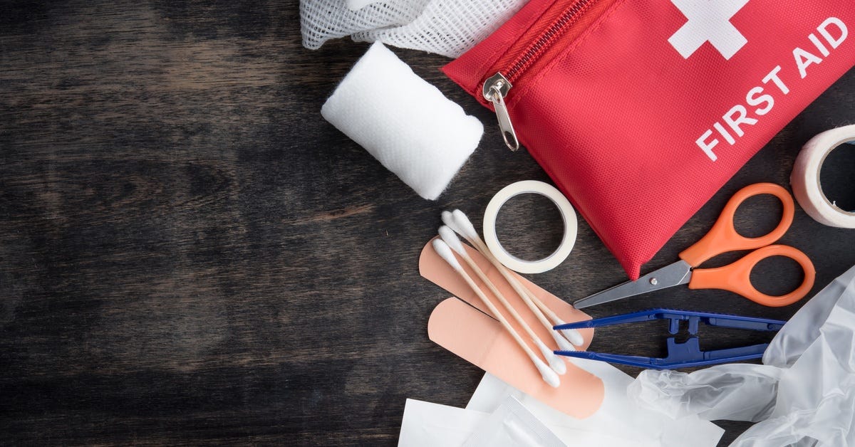 A first aid kit consisting of gauze, bandages, tweezers, and scissors is spread out on a wooden surface.