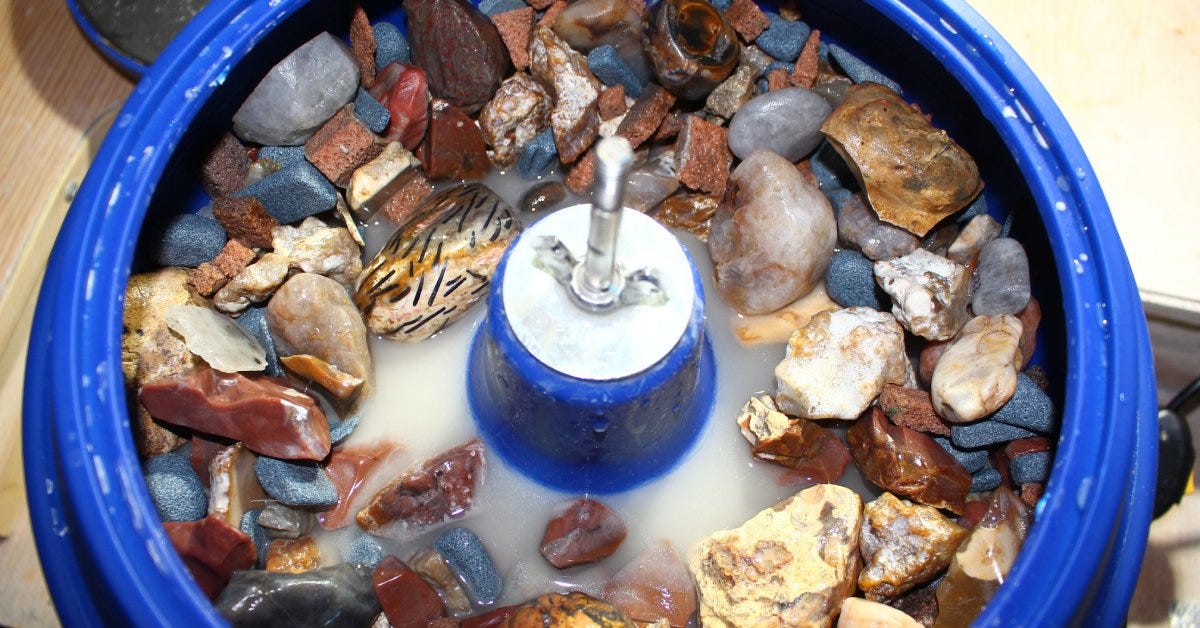 A vibratory rock tumbler bowl filled with unrefined stones and water. The rocks are various shapes and sizes.