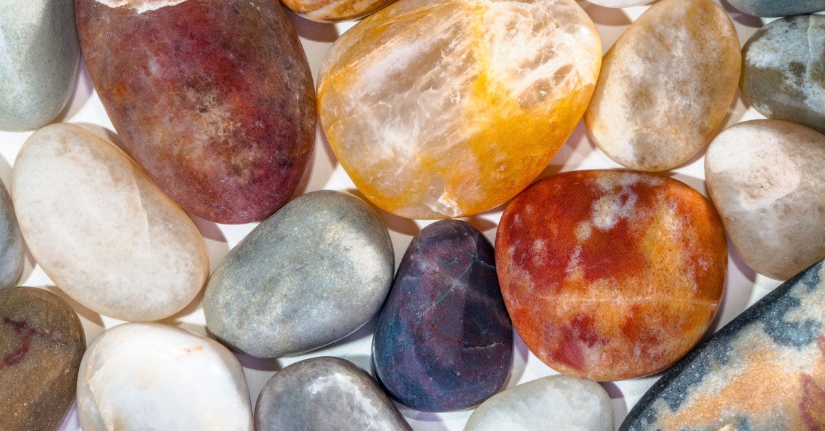 Aerial close-up of various types of stones with different sizes and colors with similar roundness placed on a white surface.