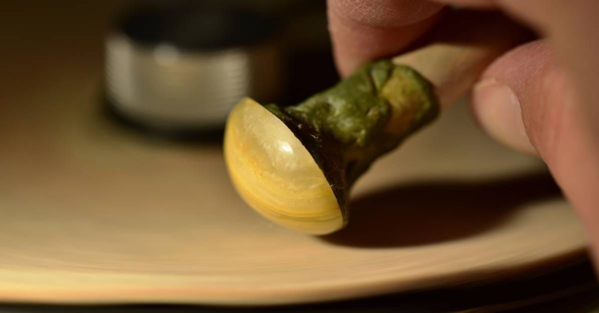 A hand is holding a wooden dop stick with a yellow round stone attached to it. The person is polishing it.