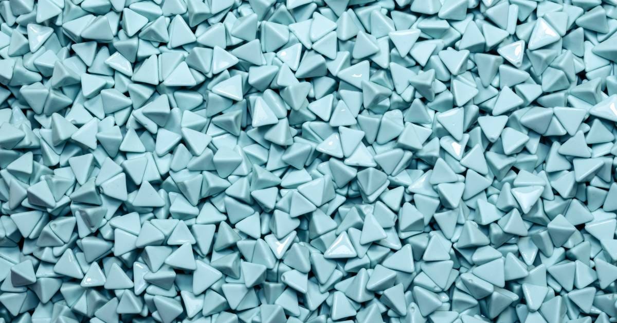 A large pile of small grit triangles of the same size fills the frame. They are light blue in color and shiny.