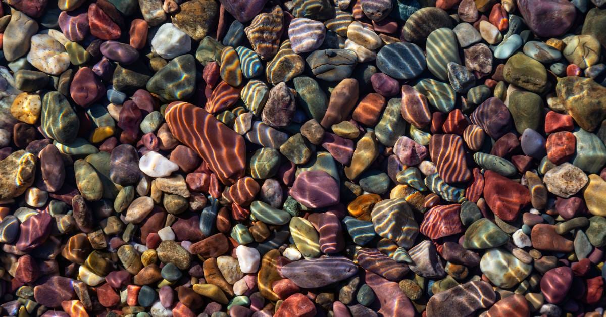 Stones of different sizes, colors, and textures inside the water with reflected light from an overhead view.