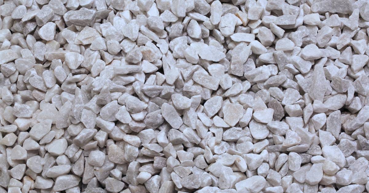 A large pile of small pebbles with different tones of gray and white are mixed together and fill the frame.