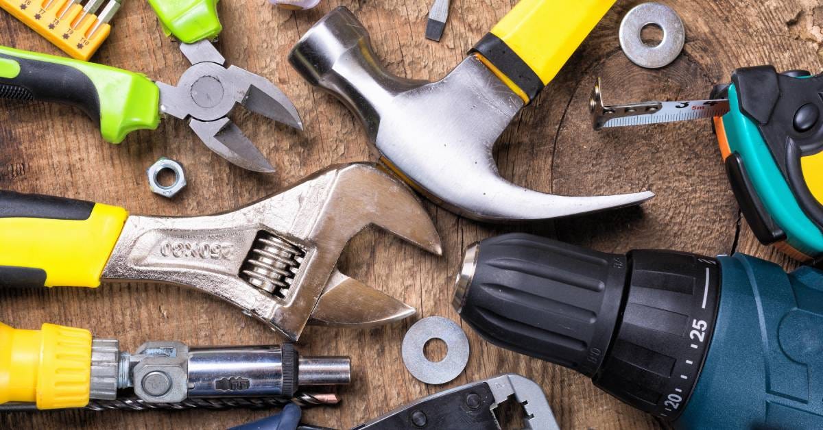 Close-up aerial view of a brown wooden table with a wrench, hammer, measuring tape, pliers, screwdrivers, and a drill on top.