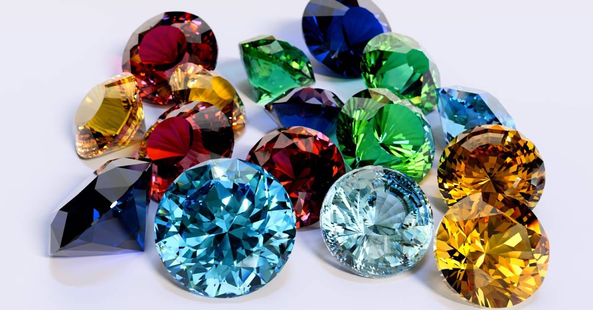 Multiple faceted gemstones cut in a round brilliant shape in shades of blue, green, and red lie on a white surface.