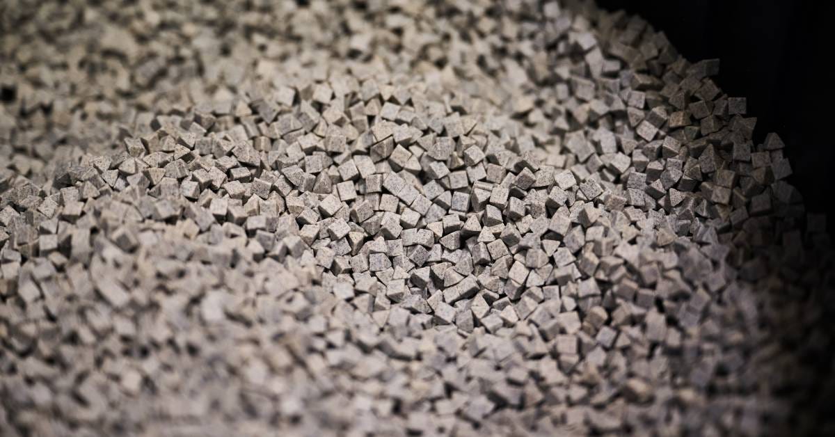 Close-up of a large pile of small grey cubic ceramic media with blurry edges and a dark background in the upper right corner.